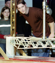 A student watches how much weight his bridge can withstand.